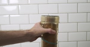 Man pulls out a dirty water pre-filter cartridge. Cartridge replacement concept. Transparent plastic flask.