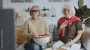 Emotional cheerful old ladies watching Tv series at home eating popcorn enjoying laughing. Generations. Elderly people. Friendship. Entertainment.