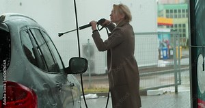 Beautiful young blonde woman washes car with spray foam and water at self-service car wash. Pretty woman is washing the car outside on the car wash self-service.
