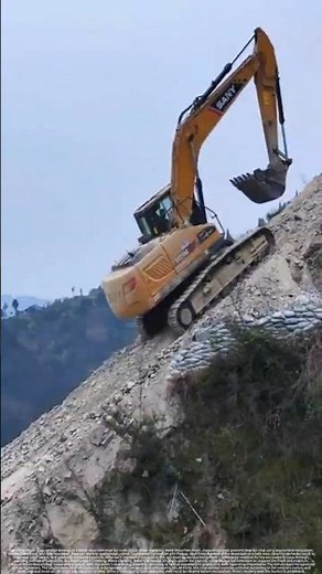 An excavator is driving on a steep mountain road – performing road repairs.