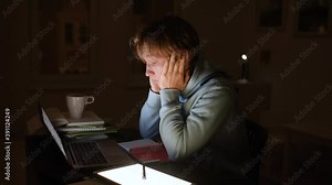 Tired teenager boy doing homework by laptop at night and falling asleep.Preparation for exams.Homeschooling, online learning, multitasking, overwork, stress - lifestyle of student while covid lockdown