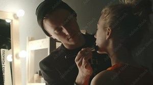 Male makeup artist applying cosmetics with brush to face of beautiful fashion model