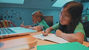 Two cute smart children doing their homework together. Little elementary kids learning with online teacher studying distant education classes from home. Self-isolation. Quarantine. Social distance.