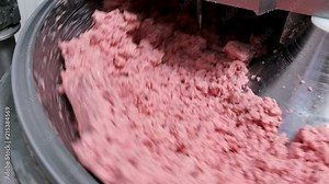 Minced meat, ground meat in a industrial chopper machine. Mixing meat and spices for making hot dogs and sausages in a food factory.