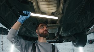 Caucasian man professional mechanic in uniform repairman male engineer working underneath car check fix problem under automobile using flashlight light vehicle diagnostics garage service auto repair