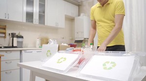 Person throwing waste into recycling bins in the kitchen. The man sorts the waste paper, plastic and glass in the kitchen for recycling and puts them in boxes.