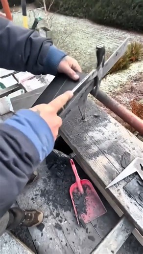 Worker using roofer's hammer to cut dark roofing shingle