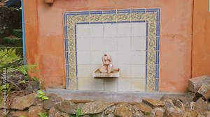 Tracking view of small tile fountain with female sculpture and rock walls with plants