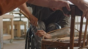 Medium shot of hardworking young Caucasian wheelchaired carpenter using hand tools to disassemble seat of old wooden chair for its further restoration, working in carpentry workshop with workmateMediu