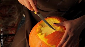 Woman carves scary face on yellow pumpkin by the knife. Hands close up. Autumn, holiday, Halloween
