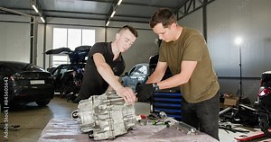 Two mechanics collaborating on the repair of an electric car engine in a modern auto service garage. Focused maintenance work on advanced automotive technology. EV repair and service concept.