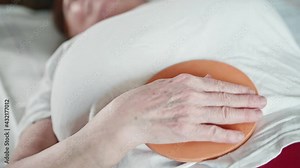 View of woman body lying on bed. Woman has Mishin coil on her belly and strokes it with her hand in clockwise fashion. Alernative medecine.