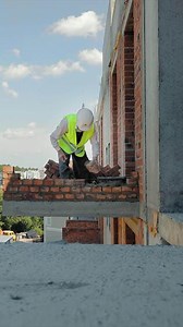Construction worker placing bricks on an outdoor ledge. A construction worker wearing a high-visibility vest and a hard hat carefully places bricks on the edge
