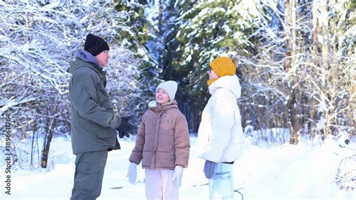 A man and two girls share a joyful snowball toss in a sunlit winter forest, laughter, motion, and warm connection amid frost-covered trees and sparkling snow.