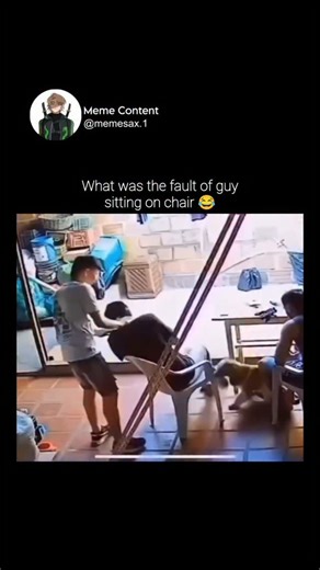 Meme Content on Instagram: "This security camera footage captures a chaotic and accidentally painful chain of events in what appears to be a patio or workshop area. The video begins with a man in a light-colored shirt trying to navigate around a person seated in a white plastic chair. As he attempts to step over or around the chair, his leg gets caught, causing him to lose his balance and stumble directly onto the seated individual. In the scramble to recover, he inadvertently kicks a large, whi