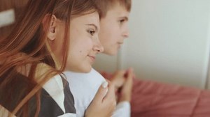Young siblings bonding while watching tv, sister resting head on brother's shoulder, sharing warm familial connection on living room couch