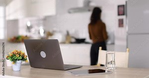 Woman putting food in microwave oven then taking smartphone and returning to laptop during work on remote project in modern kitchen at home