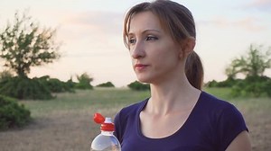 Young woman drinking water from plastic bottle at sunset