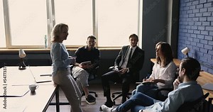 Older 50s businesswoman or company head talking standing in front of millennial staff members, makes speech, motivate to group, explain corporate strategy, take part together in briefing at workplace