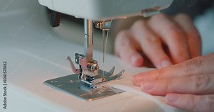 Close up of woman fingers sew on sewing machine. Details of sewing machine. Woman is overlocking textile. Workshop in sewing fabric. Creation and tailoring clothes.