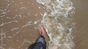 A man is walking on the beach shoreline. He is walking on the waves of the beach. Slow motion of feet walking on the beach waves.
