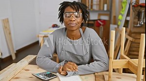 Joyful young black woman with dreadlocks rocking safety glasses, working at carpentry, flashing a beaming smile and positive approval sign, epitome of success and confidence