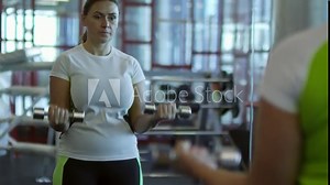 Medium shot with slowmo of middle-aged woman doing dumbbell bicep curls exercise before mirror in gym