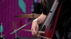 Super slow motion: woman hands playing electric cello on stage of summer open air concert - close up view. Entertainment, classical, music, culture, leisure time and art concept