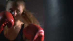Une fille est boxeuse. La fille s'entraîne dans le hall de boxe. La fille frappe un sac perforant.