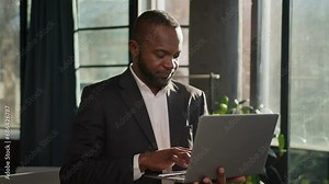 Senior specialist 50s businessman stand with laptop in sunbeams office middle-aged African American male employer working online computer data analysis adult business man looking at camera happy smile