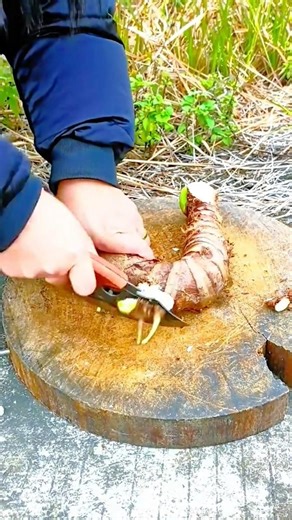 Slicing a large brown taro root into small pieces using a sharp knife on a wooden cutting board
