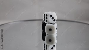 Three 6-sided dice slowly spinning on a mirrored turntable