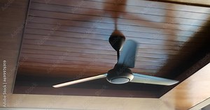 Bottom up view of a ceiling fan that is located on a wooden ceiling. The fan starts spinning and cools the air in the warm room. Air cooling using a fan.