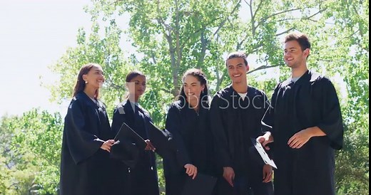 Group of graduates celebrating and throwing caps or hats into the air in tradition after university campus graduation ceremony. Smiling diverse men, women, friends graduating from college together