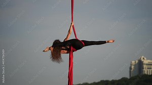 Female circus artist showing her flexibility and splits with red aerial silk on the sky background. Concept of healthy lifestyle