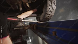 Mechanic stands in the pit and checks suspension at the car service station, suspension repair, vehicle pit, wheel alignment, Full HD Prores 422 HQ