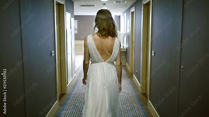 Shot from behind of a woman in beautiful white dresses passing doors in a hotel corridor.