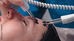 Close-up portrait of a beautiful woman with closed eyes and a skin rejuvenation machine. Salon procedures. Microcurrent therapy