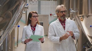 Woman and man in white lab coats working in a brewery and testing the quality of beer. Man taking beer sample for testing. Woman taking notes. Science, brewery concept.