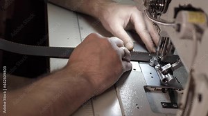 Sewing a leather belt with a sewing machine. Small family business with leather sewing, slow motion, 50 frames per second. Close-up of male hands while working in the workshop