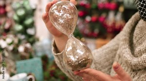Close-up of an hourglass in the hands of a woman in motion. She turns the watch over with her hands and watches the bulk material. Expiration of time before the holiday.