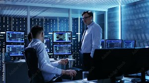 Team of Technical Moderators Have Discussion in Monitoring Room. System Control Room is full of Working Displays and Has Servers Racks. Shot on RED EPIC-W 8K Helium Cinema Camera.