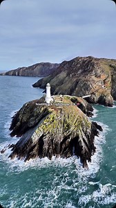 South Stack Lighthouse – Where Land Meets the Wild Waves! 🌊🏔️ Experience the stunning aerial view of South Stack Lighthouse, standing tall on the rugged cliffs of Anglesey, Wales. This iconic lighthouse, built in 1809, guards the treacherous waters of the Irish Sea, guiding sailors safely through the coastline. In this breathtaking drone footage, you can witness the mighty ocean waves crashing against the rocky cliffs, creating a mesmerizing contrast between the deep blue sea and the white lig