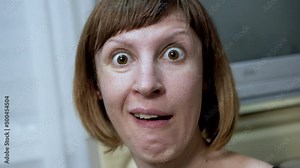 Close-up Facial Expressions of a Crazy Woman with Bulging Eyes, Crooked Teeth. A woman with wrinkles on face looks at the camera, makes a face, grimaces, moves lips, rotates eyes wide open. Behavior.