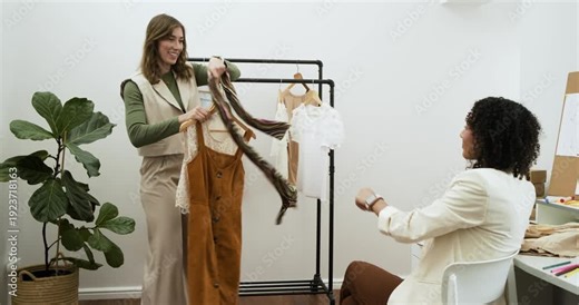 Female stylist entering left selecting dress, layering blouse for African American client in studio