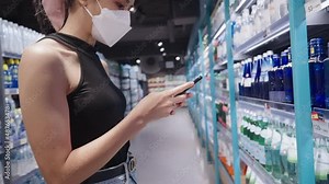 Young pretty lady wear facemask using smartphone scan qr code searching for goods products information, grocery store beverages shelves, technology for convenience service, easy and simple way to shop