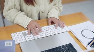 Une femme tape sur un clavier devant un ordinateur portable. Elle porte un chandail blanc et a la main sur le clavier. La scène laisse entrevoir une atmosphère concentrée et productive