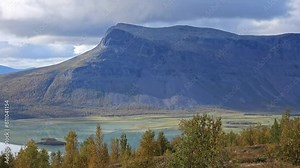 A view of a deep valley with Låjtávrre lake and high hills of Sarek National Park in northern Sweden on the long-distance hiking route the King's Trail in early autumn colors