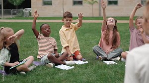 Children raising hands during outdoors class with teacher