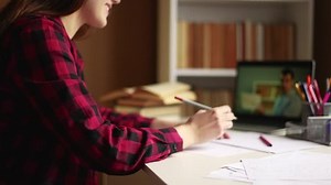 learn virtual. a teenager girl is studying remotely from a teacher online on a laptop sitting at a table next to a bookcase. distance learning education indoor concept. student on exam online